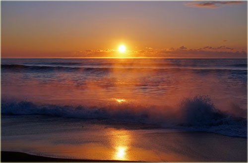 　荒々しく波しぶきが上がる海の日の出